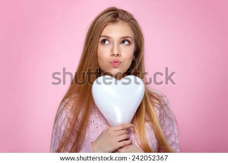 Sweet blonde woman holding a heart shaped balloon. Studio portrait over pink background. Happy birthday. Valentines Day. Joyful