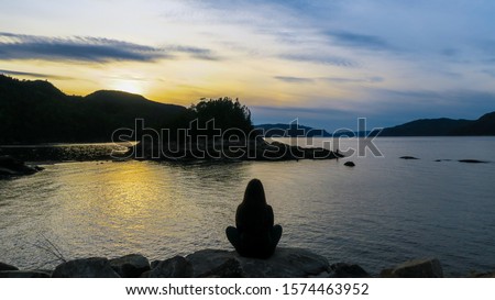 Contemplative woman sitting in a shore in front of the beautiful fjord of Saguenay at Petit-Saguenay