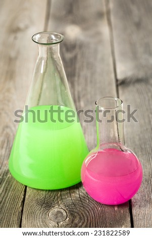 Chemical laboratory flasks with green and pink liquid. On vintage wooden table.