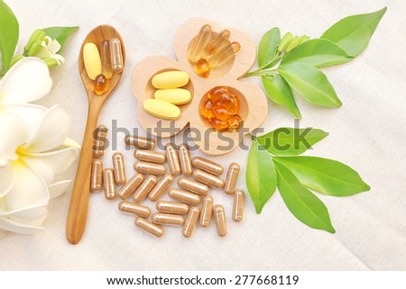 Herbal supplements and vitamins  on wooden tray and wooden spoon, decorated with white flowers and green leafs background as white cotton cloth