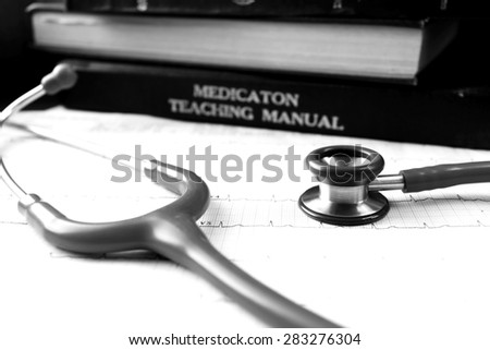 Black and white picture of stethoscope and EKG graph and medical textbooks.