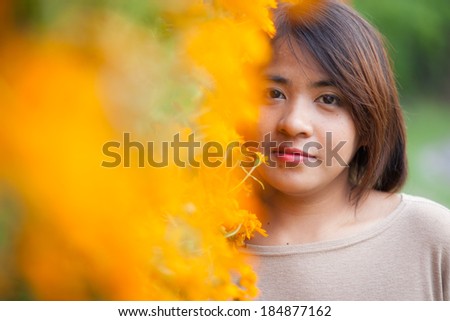 Portrait Asian woman standing near yellow flowers. Within the park area With small yellow flowers