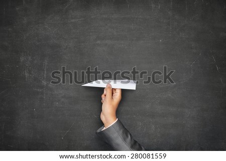 Businessman hand holding paper plane on front of vintage full frame black blank blackboard no frame