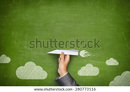 Businessman hand holding paper plane on front of vintage full frame green blank blackboard no frame and couple clouds