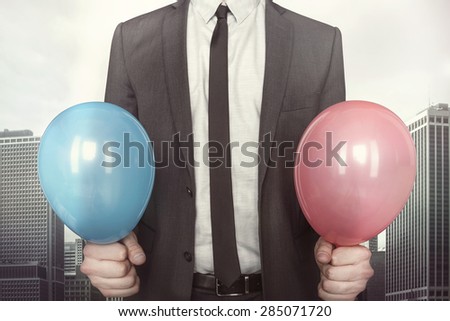 Businessman holding balloons in hands in suit on cityscape background