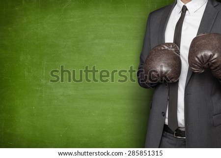 Businessman in boxing gloves and suit on blackboard background