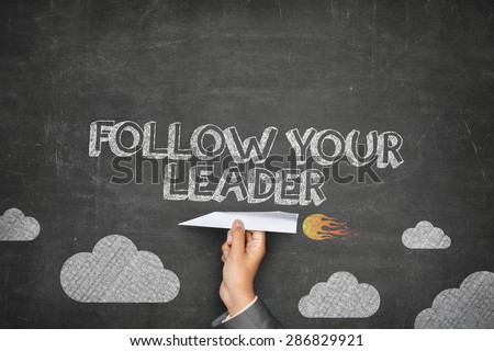 Follow your leader concept on black blackboard with businessman hand holding paper plane
