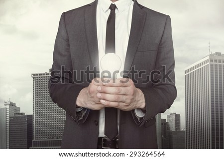 Businessman holding light bulb in hands on cityscape background