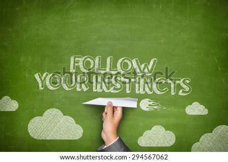 Follow your instincts concept on green blackboard with businessman hand holding paper plane
