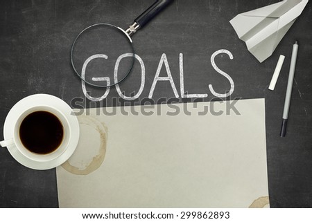 Goals concept on black blackboard with empty paper sheet and coffee cup