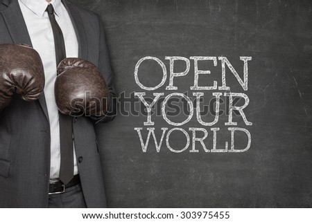 Open your world on blackboard with businessman wearing boxing gloves