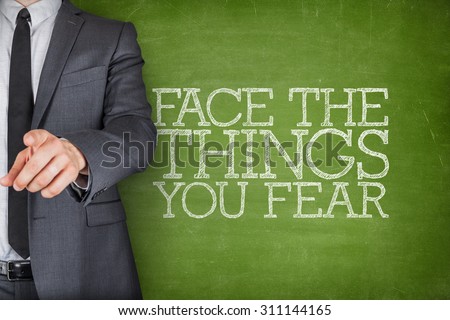 Face the things you fear on blackboard with businessman finger pointing