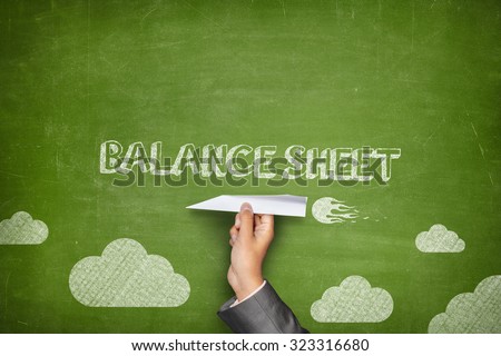 Balance sheet concept on green blackboard with businessman hand holding paper plane