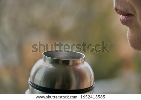 Photo of Young woman holds a thermos and drinks tea in autumn forest.
