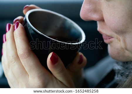 Photo of Young woman sits in the trunk of the car and holds a cup of hot drink in her hands