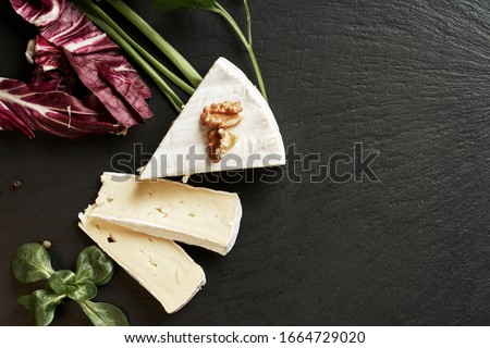 Delicious brie cheese on black background. Brie type of cheese. Camembert. Fresh Brie cheese and a slice on stone board. Italian, French cheese.