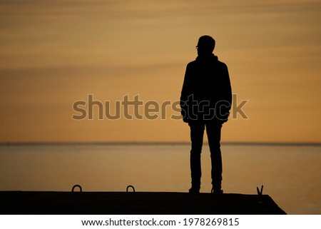 Photo of man standing on rock looking straight. Nature and beauty concept. Orange sundown. silhouette at sunset