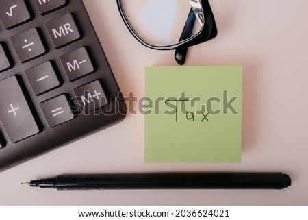 Taxes calculation concept. Closeup of word Tax written on green paper note. Time to pay taxes. Business and tax concept.
Calculating numbers for income tax return with pen, and calculator, top view. 