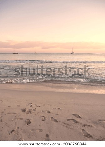 Sand beach with foot prints, sailboat in the sea in the morning sunrise light. Sea boat docked in Belearic Islands on pink sky background. Mediterranean sea. Spain, Majorca. Sunset at sea. Seascape.