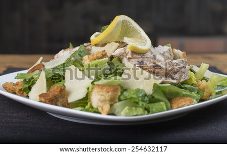 A sumptuous gluten free chicken Caesar salad on a black place mat.  The view is from the side.