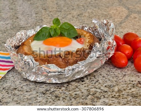 Fresh snack or dinner or breakfast, small bread with gratin cheese, vegetables, ham, tomatoes egg on the top and fresh basil baked in aluminium foil with cherry tomatoes as a side dish