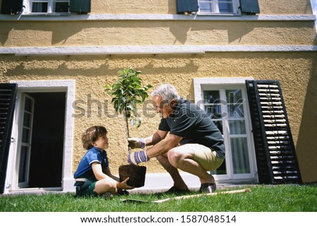 Side view of grandfather and grandson planting a tree