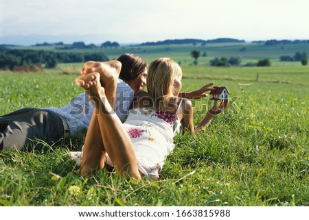 Young couple lying in field daydreaming about owning a house