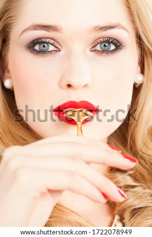 Glamorous young woman holding golden spoon in mouth, close up