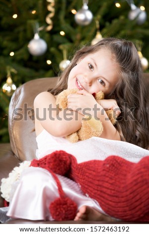 A young girl with a Christmas stocking hugging her teddy bear
