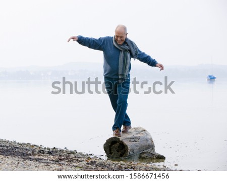 A senior man balancing on a log at the edge of a lake