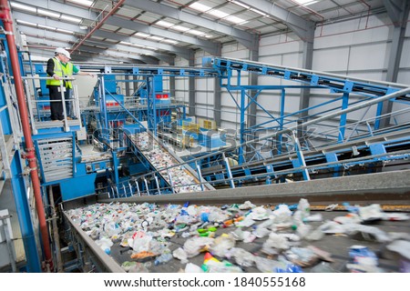 Wide shot of Businessman and worker talking on platform above conveyor belts in recycling plant