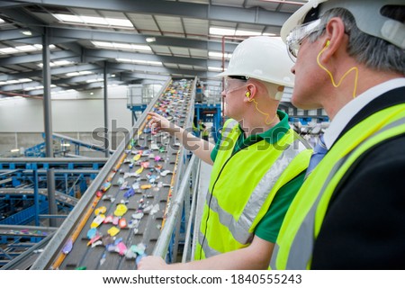 Close up of Businessman and worker talking about recycling process next to conveyor belt in recycling plant