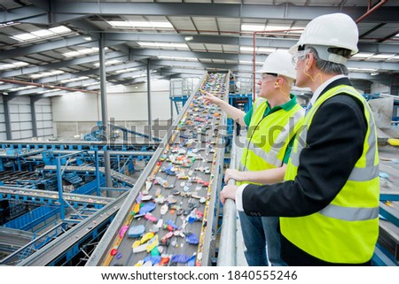 Businessman and worker talking about recycling process next to conveyor belt in recycling plant