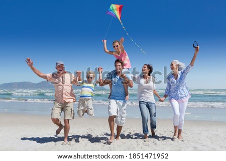 Full shot of a multi-generation family running with a kite on a sunny beach with the sea in background.
