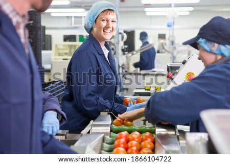 Wide portrait shot of a smiling quality control worker inspecting tomatoes on production line in a food processing plant