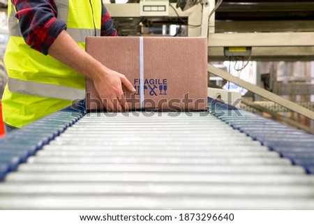 Worker in a reflector vest processing cardboard boxes on a conveyor belt at a distribution warehouse.
