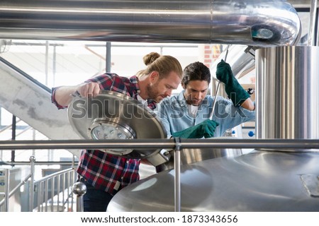 Wide shot of Brewery Workers Checking Fermentation Process In Steel Vat