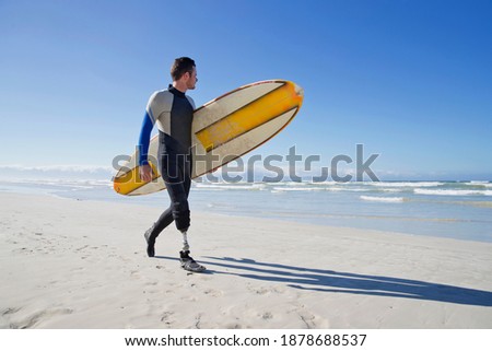 Surfer With a prosthetic Leg Walking On the Beach carrying a surf board