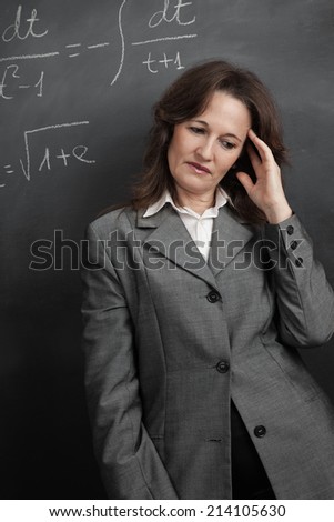 Teacher in front of the blackboard with her hand on her face and upset expression.