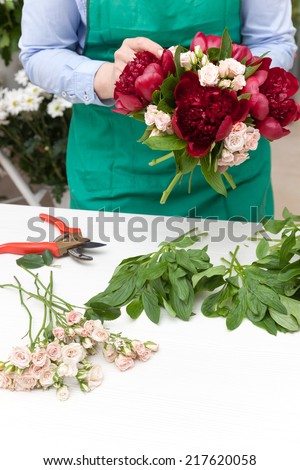 Florist making a red peonies and miniature roses bouquet. Selective focus on flowers.