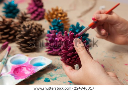 Child painting pine cones as homemade Christmas ornaments.