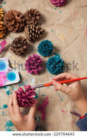 Child painting pinecones as Christmas ornaments