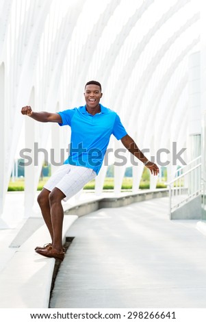 Black, African American college student pretending to surf modern architectural building