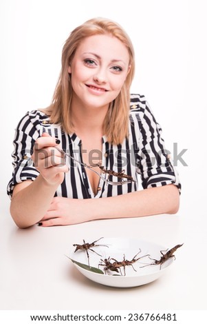 Joyful woman eating big insects with a fork in a restaurant