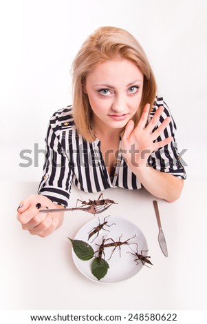 Disgusted woman eating big insects with a fork in a restaurant