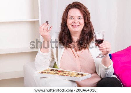 Plump woman at home eating chocolates and drinking wine - studio shoot