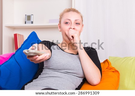 Yawning woman switching channels in front of TV at home