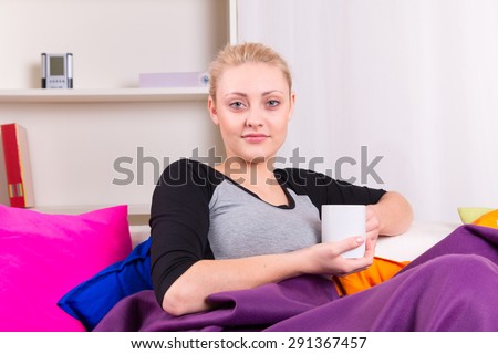 Woman on a sofa under a blanket with cup of tea