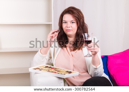 Plump woman at home eating chocolates and drinking wine
