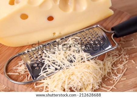 Grated cheese and grater on a wooden cutting board. Close-up.